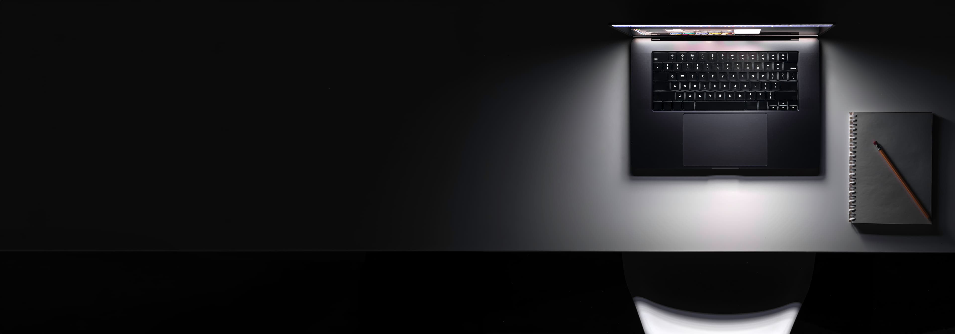 Vista superior de mesa com laptop em ambiente escuro, tela iluminada.